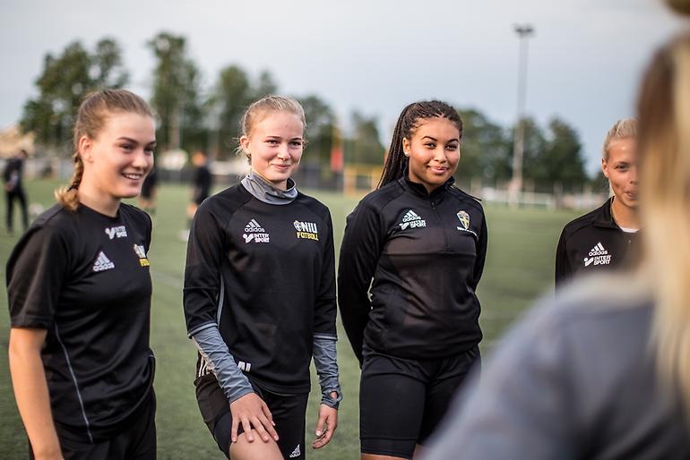 Tre glada fotbollstjejer får instruktion av tränaren.