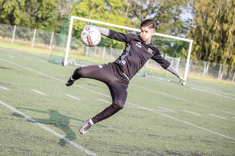 Ung fotbollskille ligger i luften och skjuter bollen i mål.